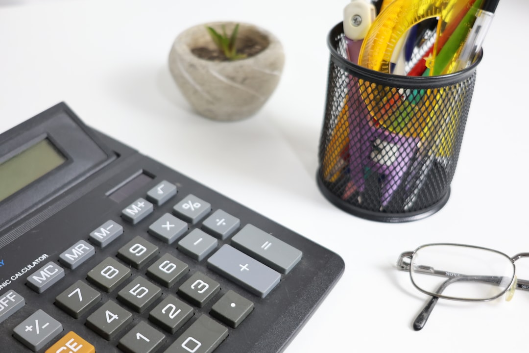 Calculator, glasses, and pens on a white desk.